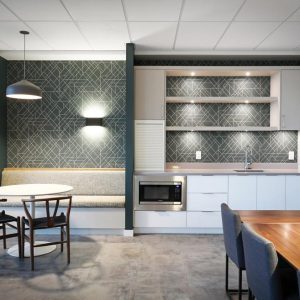 Modern kitchen and dining area with geometric-patterned backsplash, a built-in bench, a round table with chairs, a refrigerator, a microwave, and overhead and under-cabinet lighting.