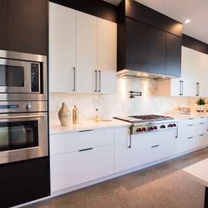 Modern kitchen with sleek white cabinets, stainless steel double oven and microwave, marble backsplash, gas stove with hood, minimalist decor, and bright lighting.
