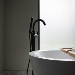 A modern bathroom with a white freestanding bathtub, a black floor-mounted faucet, and a wooden bath tray next to a frosted window, creating a minimalist and serene atmosphere.