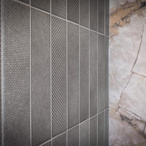 Close-up of a wall with vertically arranged textured gray tiles on the left and a smooth, light beige marble surface with brown veins on the right.