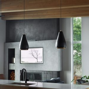 Modern kitchen with a white island, black faucet, and two black pendant lights. In the background, there’s a concrete fireplace, firewood, a TV displaying a tree, and a tall window showing greenery outside.