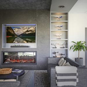 A modern living room features gray sofas, a round coffee table, a blanket, a fireplace, a wall-mounted TV displaying a mountain lake scene, shelves with model airplanes, and a potted plant in the corner.