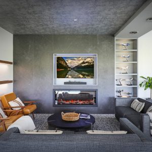Modern living room with gray sofas, two tan armchairs, a round black coffee table, and a wall-mounted TV above a fireplace. Shelves display model airplanes and a green potted plant is in the corner.